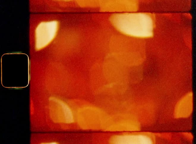 Super 8mm close up of out of focus orange and red neon lights shaping abstract bokehs with tilting upward dynamic camera movement providing contrast as modern art transition overlay or fill material