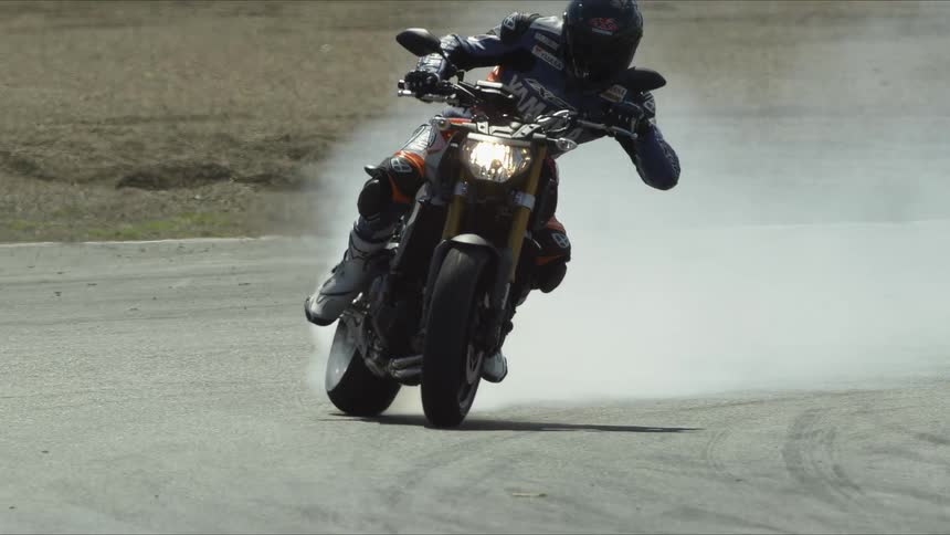 A motorcycle racer slides across an asphalt track in slow motion