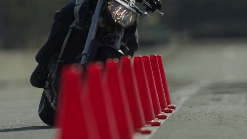 A motorcycle rider is driving through an obstacle course made of red cones