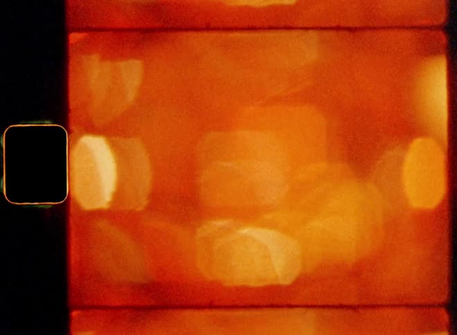 Countless orange and red light spots from a glowing chain of lights shine brightly but are out of focus and very blurry on vintage 8mm film with a nostalgic vibe creating an abstract art collage with panning or sidewise camera motion