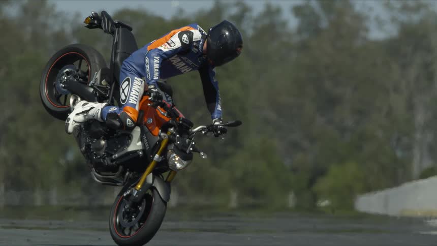 A motorcycle rider in a race suit doing a back wheelie on the pavement