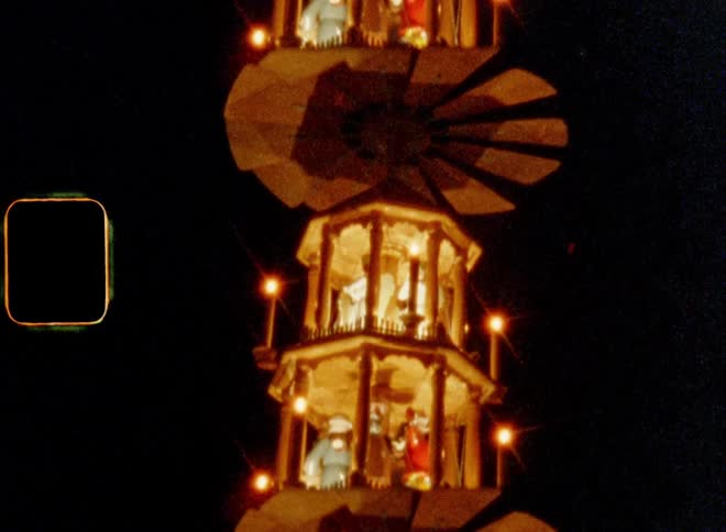Multiple clockwork Christmas figurines rotate on different levels of illuminated tower at night in a theme or amusement park lit up by candles and warm lights during winter time or advent season while Yuletide or X-mas celebration