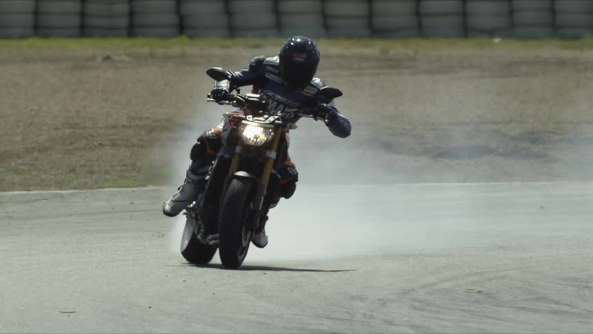 Motorcyclist speeds motorcycle around curve on track burning rubber