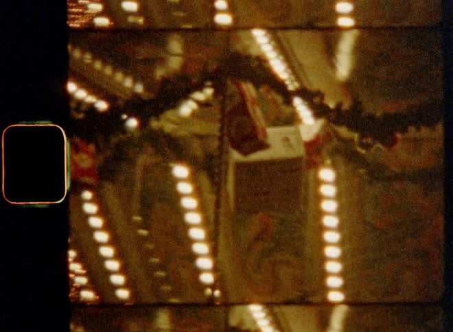 Handheld dynamic 8mm film footage of spinning or turning carousel or amusement ride on Christmas market that is decorated with countless lights and a few hanging wrapped gift boxes for a happy and loving holiday atmosphere and festive vibes