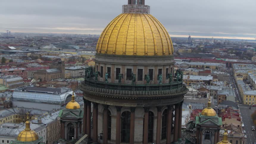 An aerial orbiting view of a building dome roof with a dense city in the background