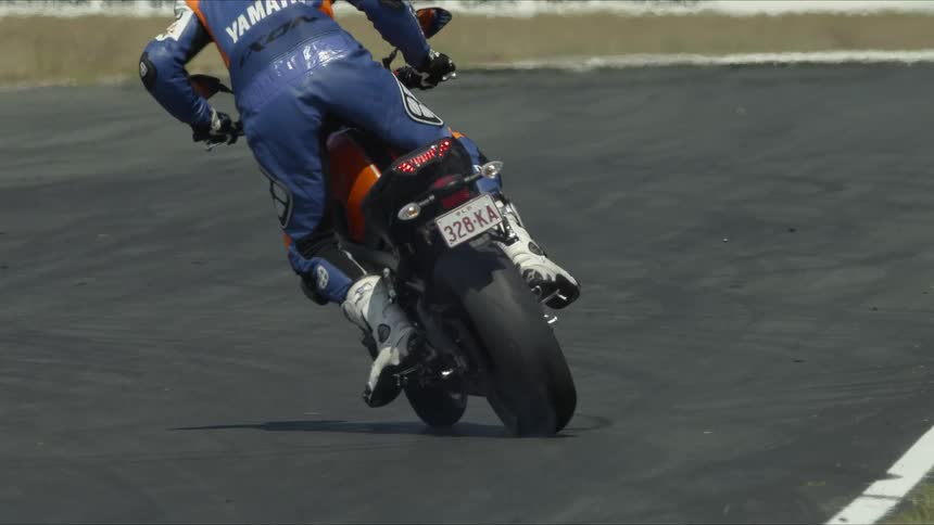 A person wearing a racing suit drives around a motorcycle and burning out on the pavement
