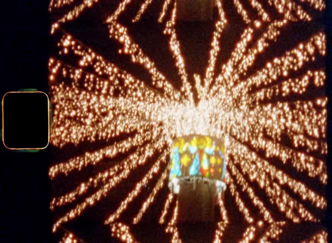 Tilting shot of millions of warm glowing lights shine in the shape of a star in front of the dark night sky connected by a centre column with a colorful light source with angels and Christmas design on 8mm with vintage film burn