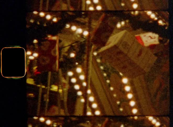 Lights are glowing and wrapped Christmas presents are hanging on a turning carousel in motion with rotation and bright shining chains of light in an amusement park during advent time and holiday season for a carefree and festive mood on vintage 8mm film