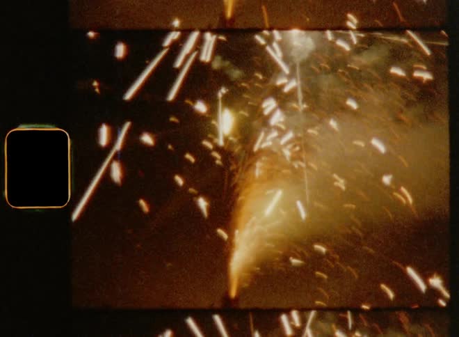 Super 8mm close up of bright sparks shooting from fireworks container sitting on the ground at night
