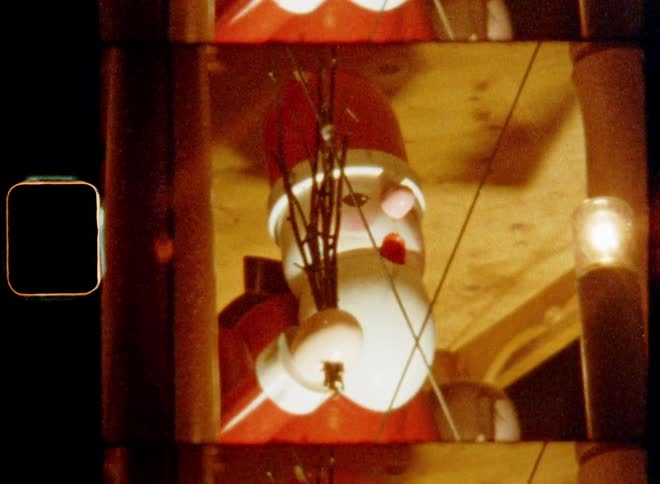 A large statue of Santa Clause or St Nicholas holding twigs or branches rotating around on a merry go round or spinning pyramid on a Christmas market or fair with decoration on nostalgic 8mm film creating a heart-warming and festive mood