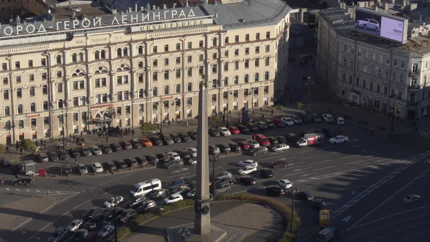 Heavy traffic drives through a roundabout outside a large city building