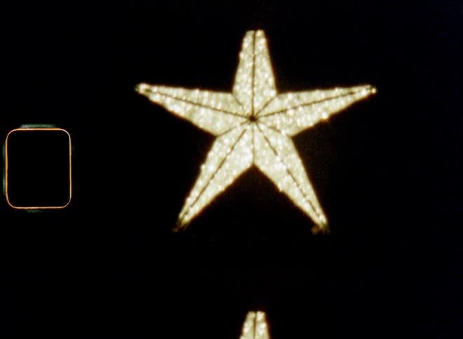 Handheld dynamic 8mm film footage with tilting upward camera movement of large decorative star shines outside of town house as symbol for the Christian morning star that is shining bright in a dark and cold winter night illuminating the black sky