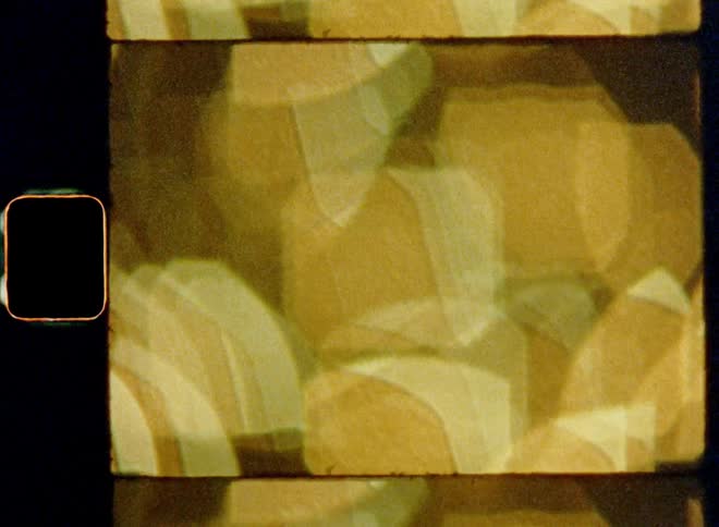 Retro or vintage Super-8 mm film footage shows a bunch of blurry lights from a decorated Christmas tree creating golden or yellow bokehs that are clustered together with downward diagonal camera movement