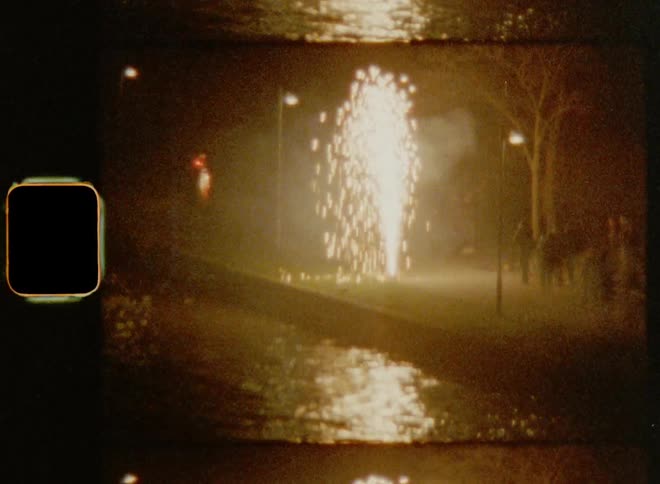 Group of people watching a large fireworks sparkler creating a bright light fountain and a reflection in the water next to a shoreline