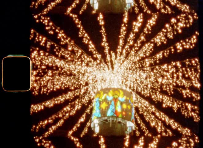 A tall pole or column has colorful images of angels on a bright X-mas light with dozens of strands of lights hanging from it shining and glowing with warm golden light and star design for festive holiday spirit in town on Christmas eve on vintage film