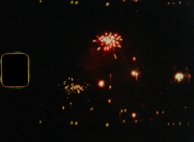 Fireworks explode in the night sky above a town on 8 mm film