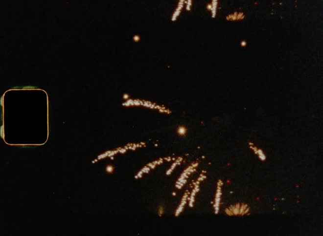 Super 8 mm film footage of fireworks going off in the night sky flashing and flaring