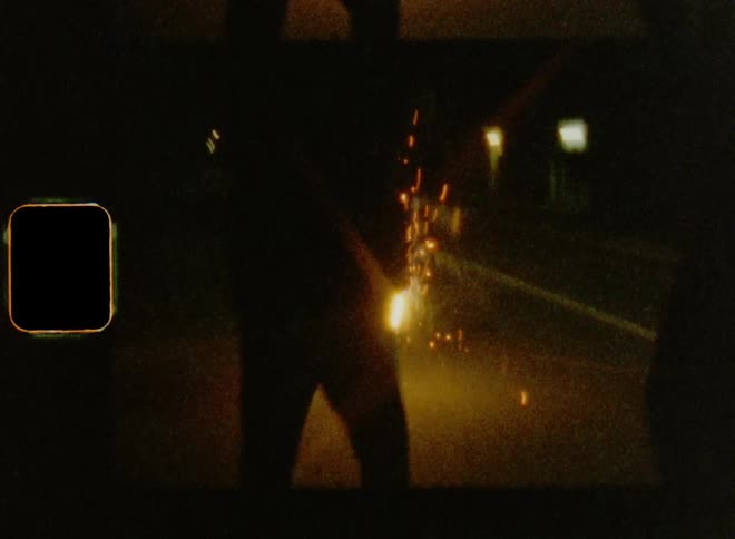 Young adults dancing and cheering careless and happy during a night time celebration on the street with sparkling fireworks on 8mm film