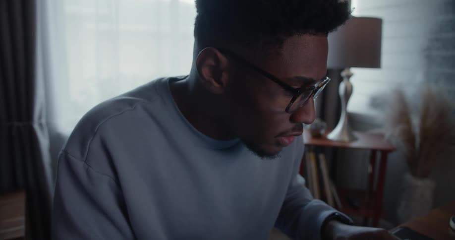 Close up of a young man wearing glasses working on a laptop at home