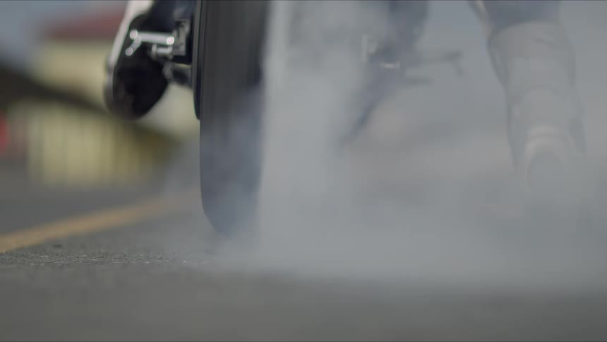 A motorcycle rider burns rubber with their back tire and leaves a skid mark as they lift their feet off the ground and take off