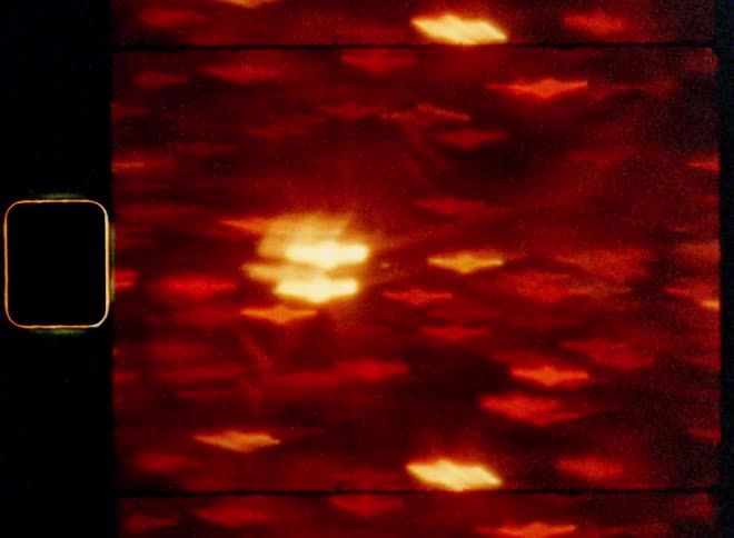 The vintage 8mm film camera moves from left to right past a large number of gleaming orange lights creating a creative and modern texture or pattern shaped by bokehs of many city lights with retro lens flare