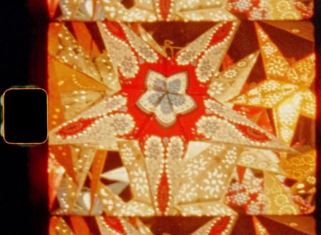 Handheld 8mm film footage of glowing paper stars and holiday decoration lanterns shine in a Christmas display at night illuminating the darkness of winter time as symbol for the Christian morning star for a festive and cosy mood