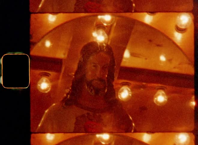 Dynamic handheld 8mm film of the hand of a figure or sculpture of Jesus Christ appears on a moving carousel with many bright glooming lights causing lens flare representing the holy spirit of Christianity and Christian faith on Christmas Eve
