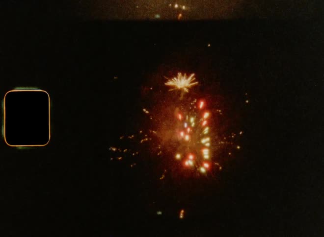 Red and gold sky rockets explode in the dark night sky during New Year’s Eve fireworks show on 8mm film