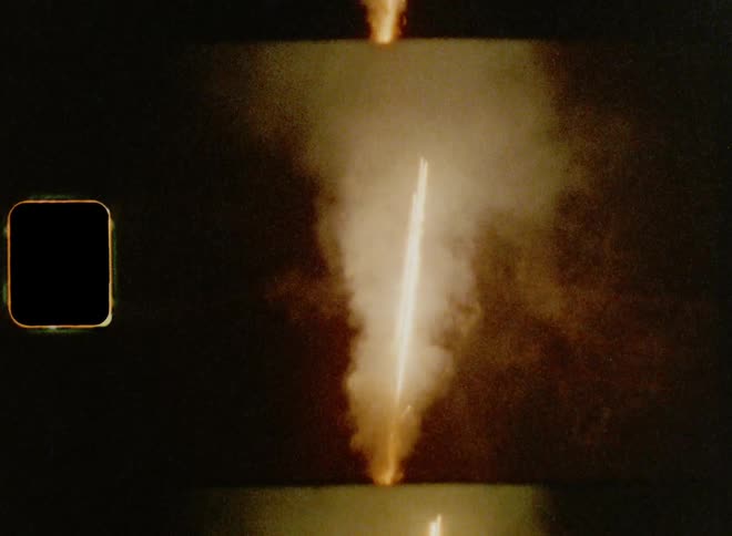Man standing on a street with cap and coat sets off fireworks up into the sky at night on vintage film