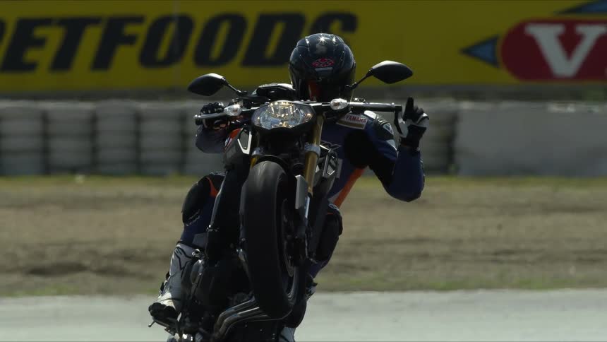 A person on a motorcycle does a wheelie and makes a hand gesture while riding