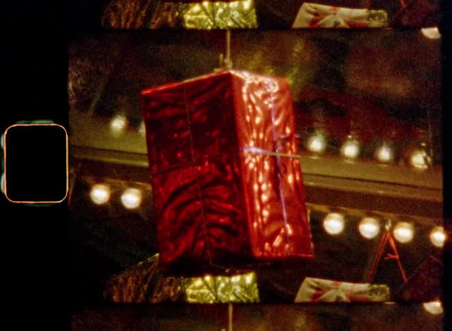 Light shines on a red wrapped X-mas or birthday present hanging and turning as a surprise in a holiday display on a Christmas fair or market celebrating the winter holiday season with festive atmosphere and cosy evening mood at night time