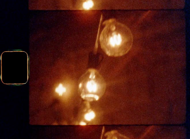 Close up of bright incandescent light bulbs hanging from the ceiling connected by an electricity cable providing power causing glare and lens flare on vintage 8mm film with a nostalgic vibe and dynamic handheld camera movement for moody lighting