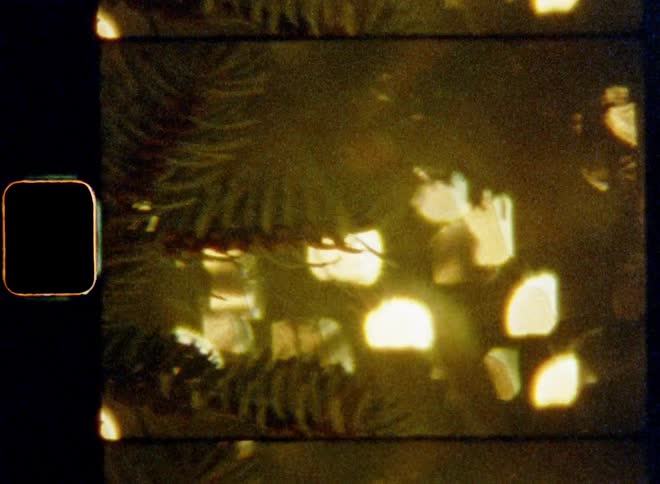 Bokehs of warm golden lights shine through pine needles of a decorated Christmas tree during advent season or X-mas evening creating holiday vibes and a festive and cozy atmosphere on vintage 8mm film with a nostalgic vibe
