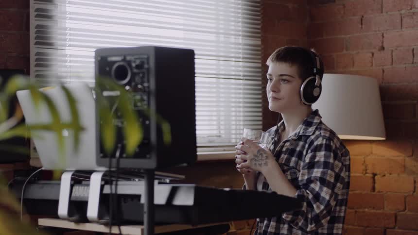 Woman wearing headphones holds a glass of water and looks at a laptop