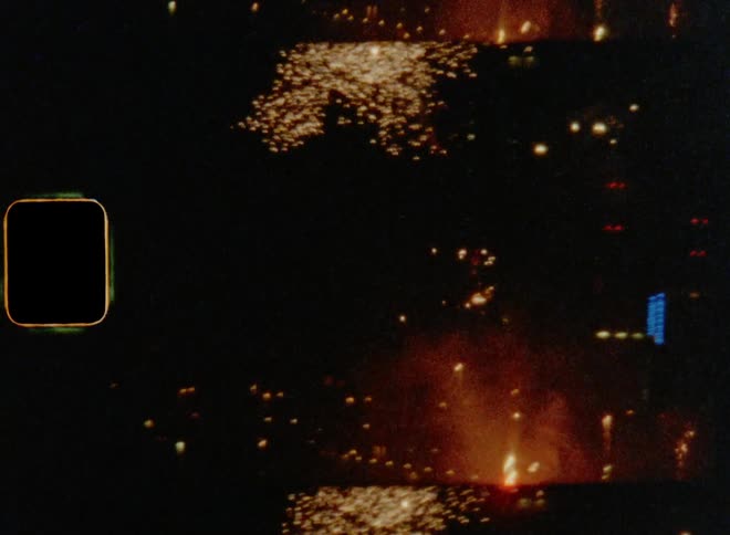 Multiple fireworks rise into night sky above cityscape and explode on Super 8 mm film