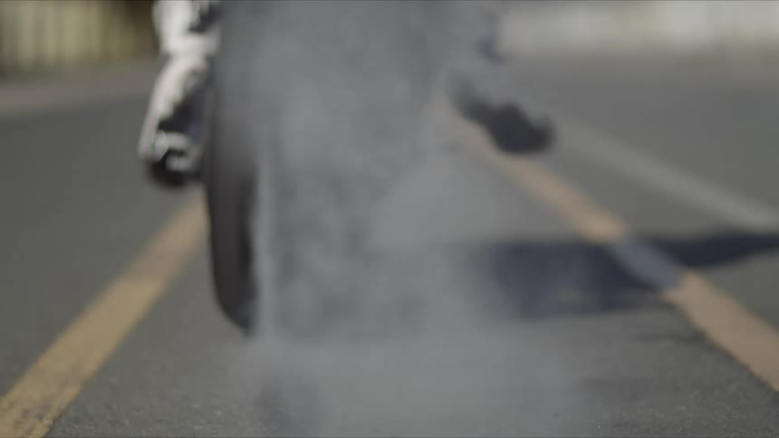 A motorcycle racer speeds away on an asphalt track while burning rubber