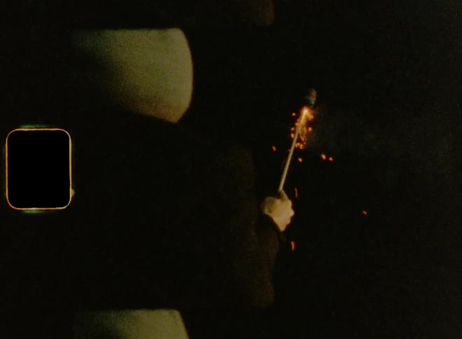 A man is standing outside holding a bottle rocket as he lights the wick and it sparks in the darkness before it takes off into the night sky