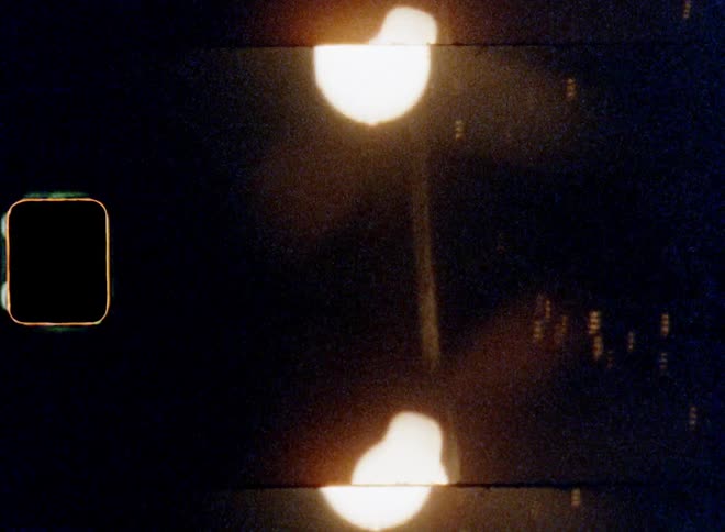 Dynamic handheld 8mm film footage of bright shining electric bulbs of a chain of lights from the street lamps or city lighting illumining the dark night sky in a town during nighttime with retro lens flare