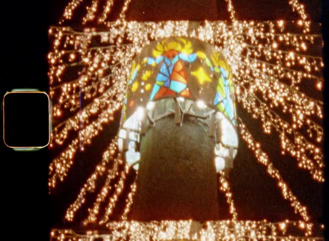 Handheld dynamic 8mm film footage with upward tilting movement of glowing light chains in the shape of a star pattern lighting up and brightening the dark night sky on a cold December evening on a Christmas fair with festive holiday vibes