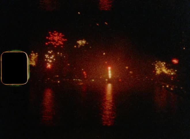 8mm wide shot of many colorful fireworks shooting into the air and exploding in the night sky along the coast
