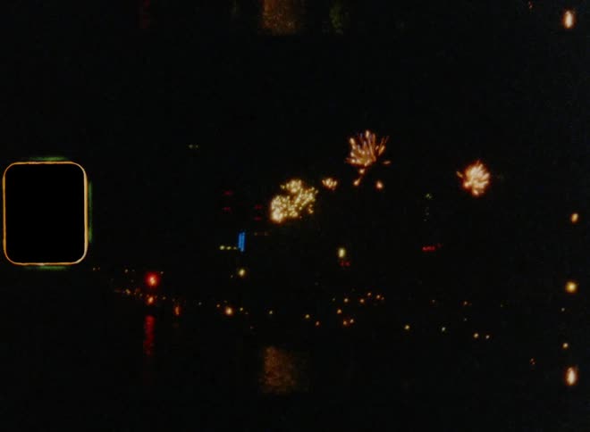 Fireworks fly into the dark sky at midnight over a skyline of a metropolis with a colorful reflection on the river