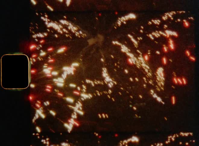Close up of large fireworks flashing and flaring in the night sky on nostalgic 8mm film