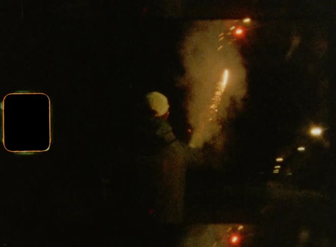 A man wearing a baseball cap holding a sparkler and letting it shoot off fireworks into the night sky