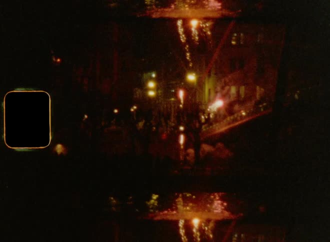 Several fireworks are fired off from outside a building next to a bridge over a river