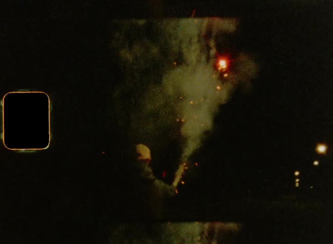 A man is walking down a street and firing a roman candle at night on Super 8mm film