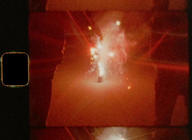 Two people watching fireworks crackers explode on the street during a night time celebration