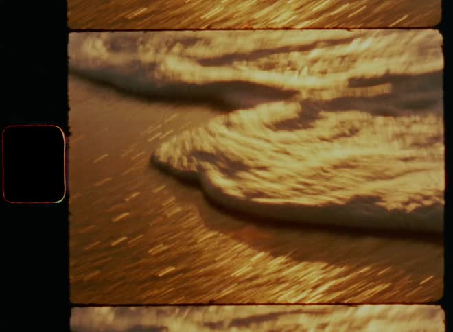 Waves rolling onto the sandy beach as foam flows over the wet sand while the warm setting sun is shining and reflecting on the water with bright glare on a summer evening with beautiful light