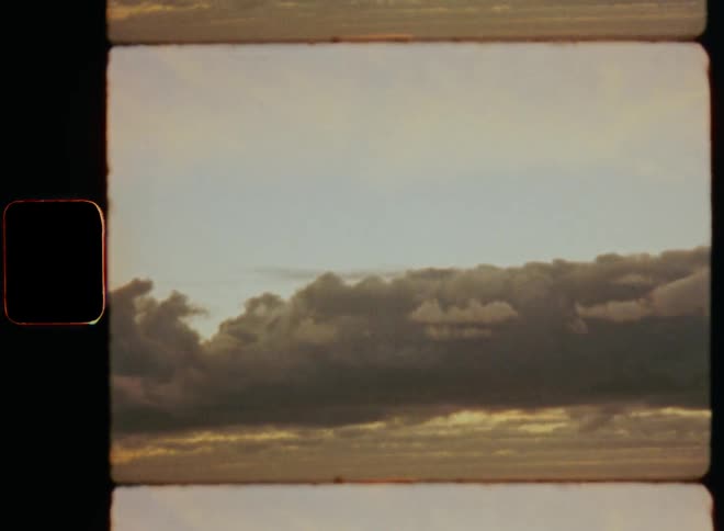Big dark clouds hover in the sky above relatively calm ocean waters during last daylight after sunset at the beach with upward tilting camera movement