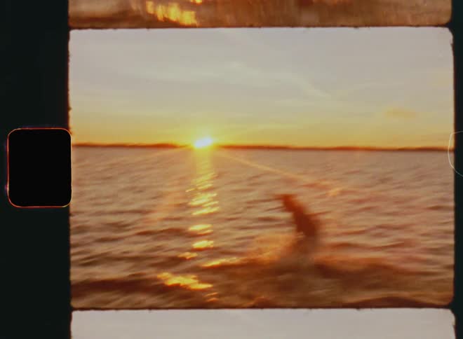 A person running into a Handheld dynamic 8mm film footage of a young Caucasian man cheering and running over the beach into the sea and jumping into the water with carefree and happy summer vibes as the sun sets at the horizon