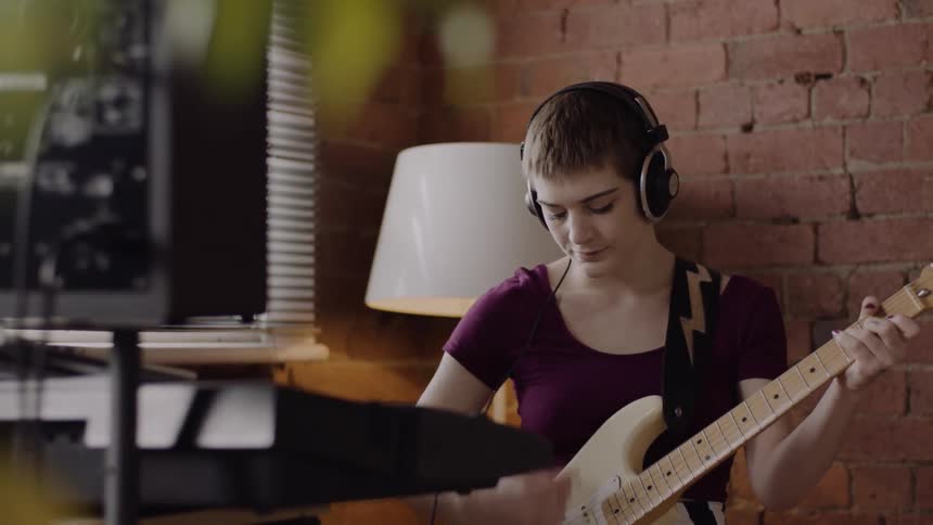 Woman wearing headphones plays the guitar